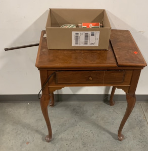 (1) ANTIQUE SINGER WOODEN SEWING MACHINE TABLE, WITH (1) BOX OF SINGER SEWING SUPPLIES INCLUDING (1) SINGer ZIGZAG ATTACHMENT, (1) SINGER AUTOMATIC ZIGZAGGER, (1) PACK OF SINGER SEWING NEEDLES, AND MORE