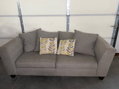 GRAY COUCH (7’ x 2’ 8” x 2’ 5”)WITH 4 BIG PILLOWS (1 IS REVERSIBLE), 2 ACCENT PILLOWS (1 FOOT REPAIR OR REPLACE) AND CUSTOM SOFA TABLE WITH BUILT-IN OUTLET WITH USB PLUS SIDE SHELVING