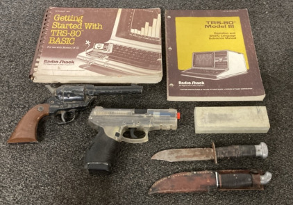 (1) RADIO SHACK TRS-80 MODELL 3, OPERATION AND LANGUAGE REFERENCE MANUAL, (1) RADIO SHACK “GETTING STARTED WITH TRS-80 BASIC, AND (2) KNIVES, (1) TAURUS BB GUN, (1) DAISY BB GUN