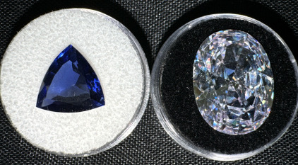(1) 29.30 Carat VVVS White Sapphire Faceted Oval Cut AAAA Gemstone (1) 9.40 Carat Blue Tanzanite Faceted Trillion Cut Gemstone