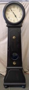 Howard Miller Nashua Floor Clock 615005 in a Worn Black Finish With a Visible Antique Brass Pendulum Viewed Through a Glass-Covered Cutout in the Front Hinged Door With A Lock N Key