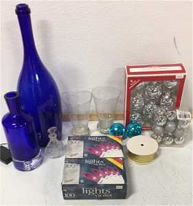 (1) large blue Glass Bottle (2) Tall Cup W/ bedazzled Base (2) Violet string Lights (1) Blue Glass Bottle W/ Fairy Lights, Ornaments and tinsel